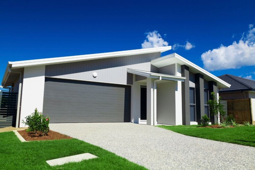 Modern single-storey home facade with a double garage, exposed aggregate driveway and neat green lawn-